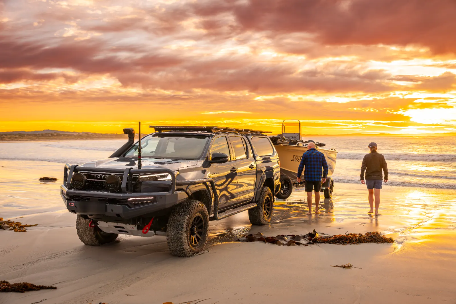 Toyota Hilux with roof rack towing a boat on a beach at sunset